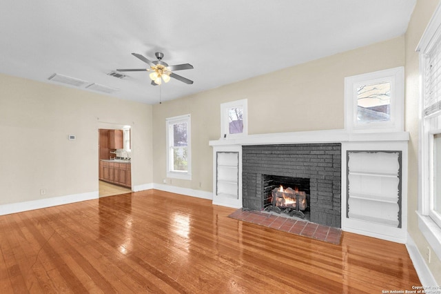 unfurnished living room with visible vents, baseboards, a ceiling fan, wood-type flooring, and a brick fireplace