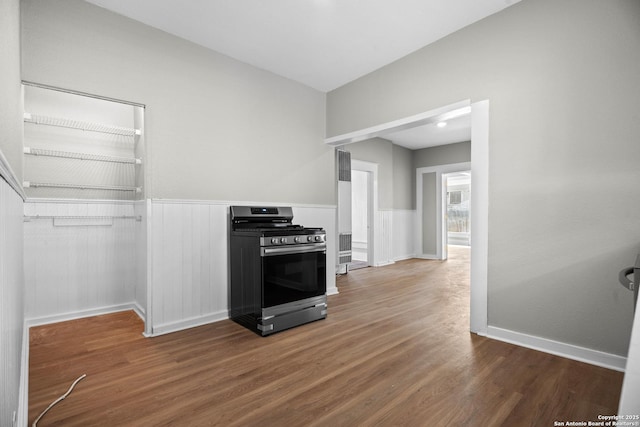 kitchen with stainless steel range with gas cooktop, wainscoting, baseboards, and wood finished floors