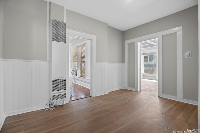 unfurnished room featuring a wainscoted wall, plenty of natural light, a heating unit, and wood finished floors