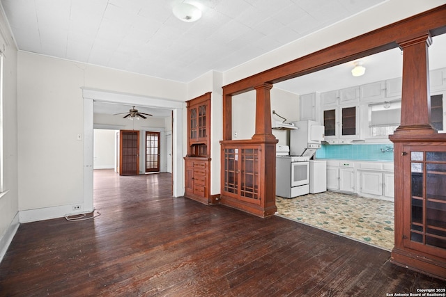 unfurnished living room featuring dark wood-type flooring, decorative columns, baseboards, and ceiling fan