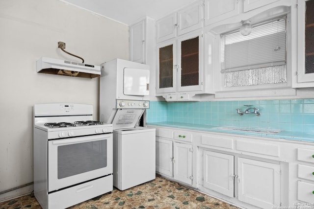 kitchen with under cabinet range hood, white range with gas stovetop, stacked washer / dryer, light countertops, and decorative backsplash