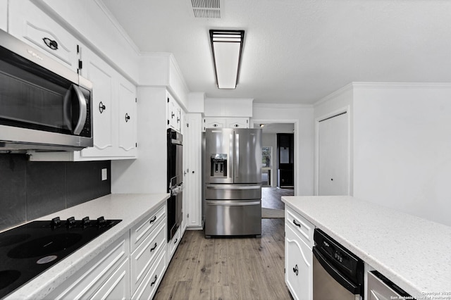 kitchen featuring stainless steel appliances, visible vents, light wood-style floors, ornamental molding, and white cabinets