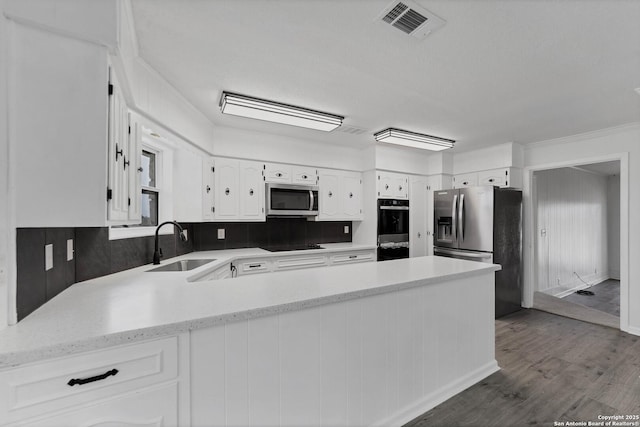 kitchen featuring visible vents, appliances with stainless steel finishes, a peninsula, white cabinetry, and a sink