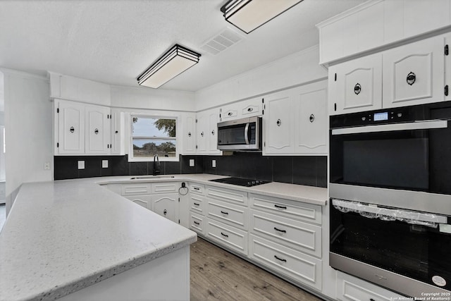 kitchen featuring visible vents, white cabinets, stainless steel appliances, light wood-style floors, and a sink