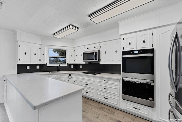 kitchen with stainless steel appliances, visible vents, white cabinetry, a sink, and a peninsula