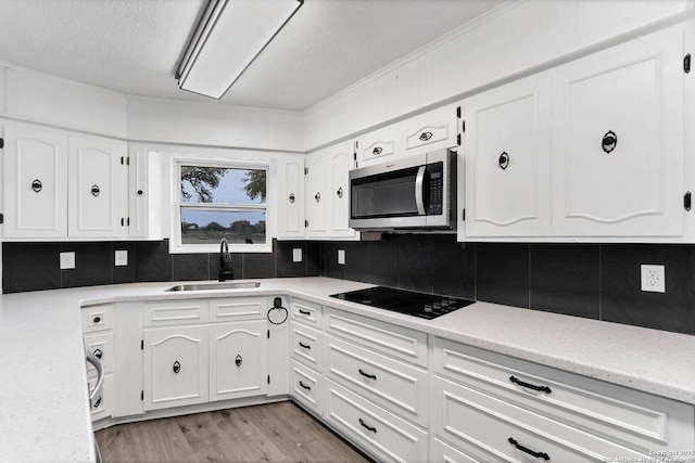 kitchen with black electric stovetop, stainless steel microwave, decorative backsplash, and a sink