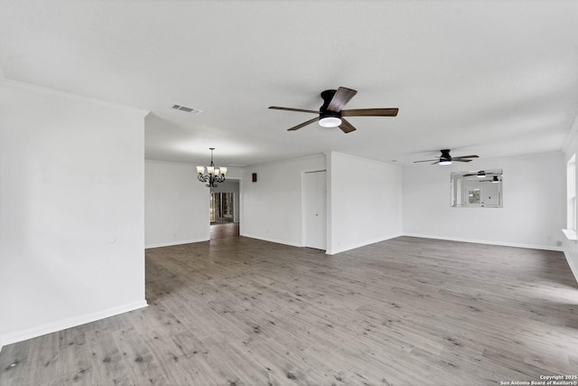 empty room featuring visible vents, ornamental molding, wood finished floors, baseboards, and ceiling fan with notable chandelier