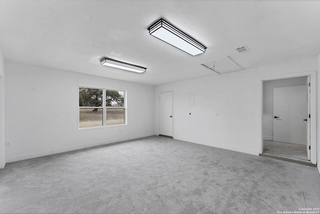 spare room featuring carpet floors, attic access, visible vents, and baseboards