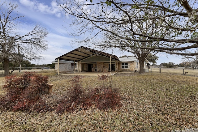 rear view of property featuring stone siding and fence