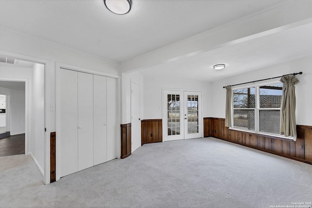 unfurnished bedroom featuring visible vents, french doors, a closet, wainscoting, and carpet