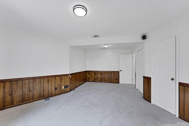 unfurnished room featuring wood walls, wainscoting, carpet flooring, and visible vents