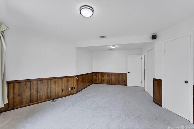 spare room featuring carpet, wood walls, wainscoting, and visible vents