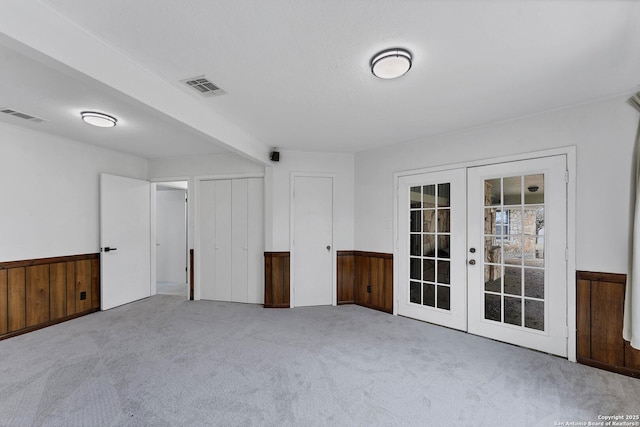 carpeted empty room featuring wainscoting, visible vents, wood walls, and french doors