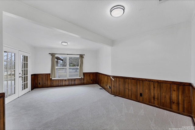 carpeted spare room featuring french doors, wood walls, and wainscoting