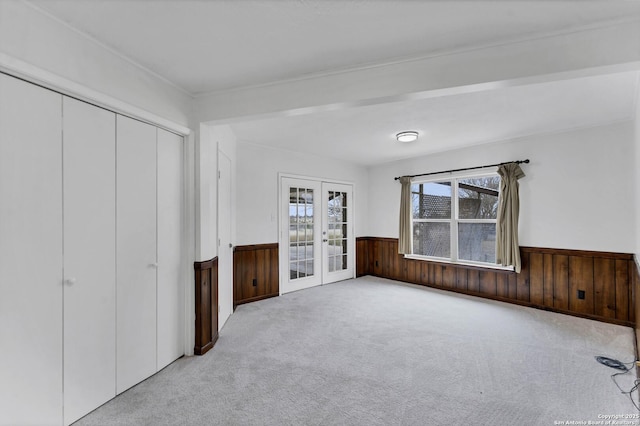 unfurnished bedroom with wooden walls, wainscoting, carpet, french doors, and a closet