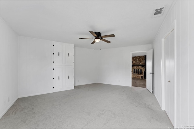 carpeted empty room featuring a large fireplace, visible vents, and a ceiling fan