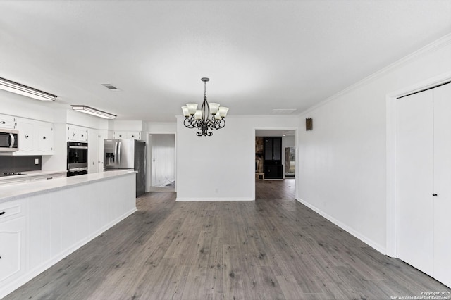 unfurnished living room featuring a notable chandelier, wood finished floors, visible vents, baseboards, and ornamental molding