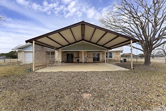 rear view of property with stone siding, fence, a carport, and a patio