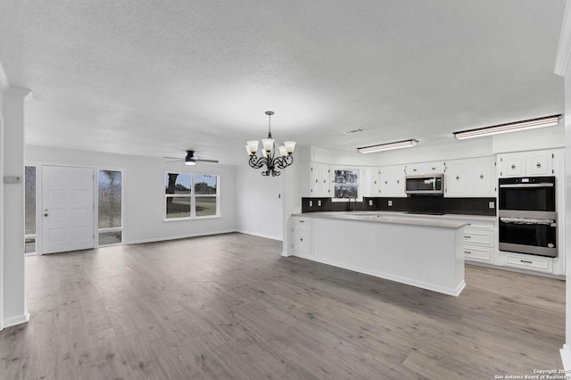 kitchen featuring light wood-style floors, double oven, stainless steel microwave, and white cabinets