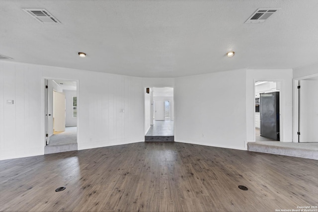 empty room with wood-type flooring, visible vents, and baseboards