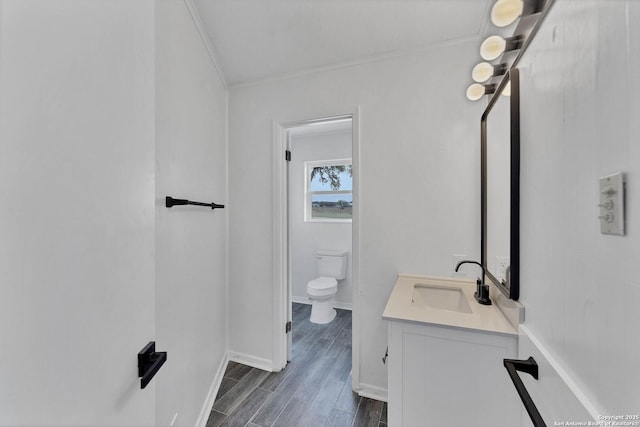 bathroom featuring crown molding, toilet, vanity, wood finished floors, and baseboards