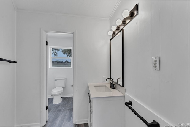 bathroom with toilet, wood finish floors, vanity, baseboards, and crown molding