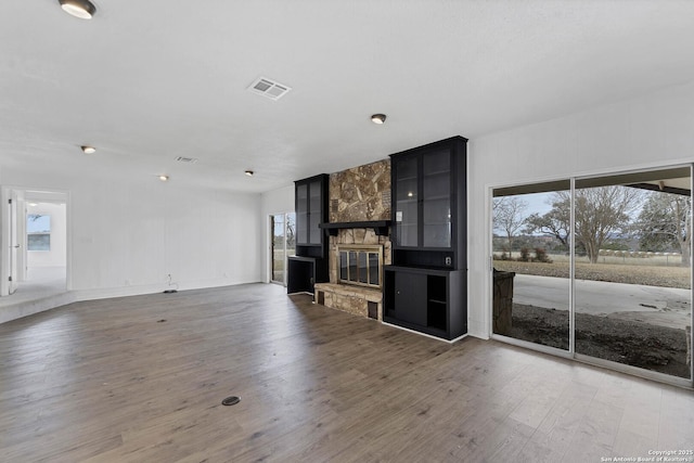 unfurnished living room with visible vents, a stone fireplace, and wood finished floors