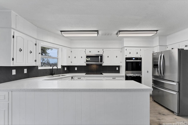 kitchen featuring white cabinetry, a sink, light wood-type flooring, a peninsula, and black appliances