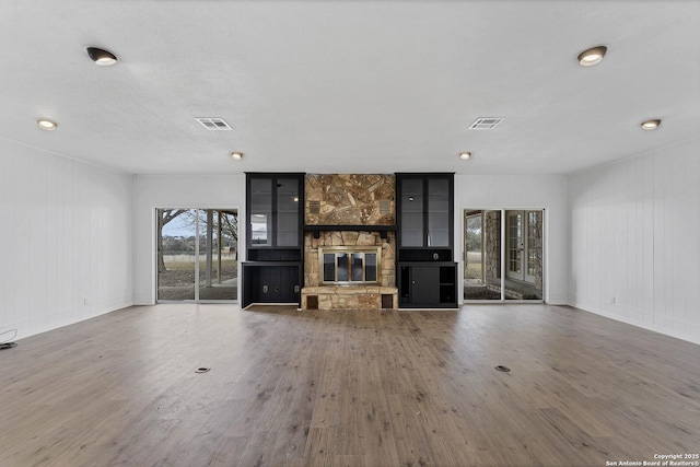 unfurnished living room with visible vents, wood finished floors, and a stone fireplace