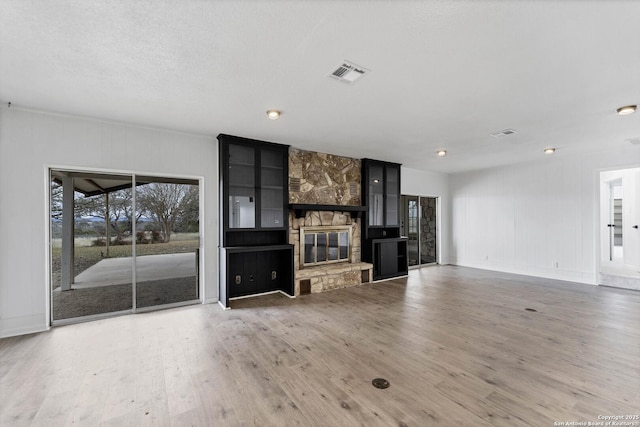 unfurnished living room featuring visible vents, wood finished floors, and a stone fireplace