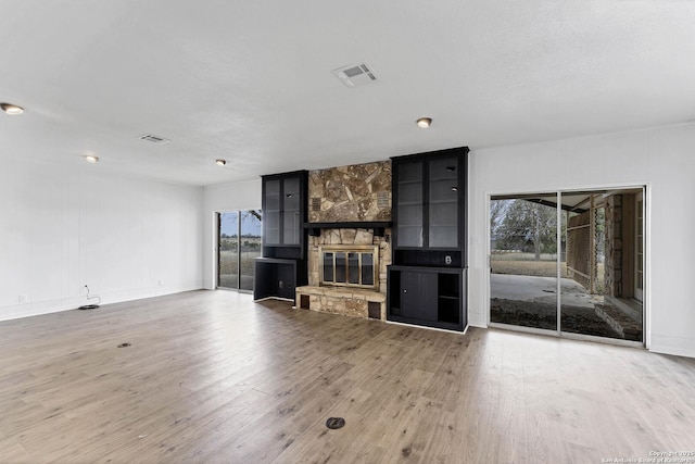 unfurnished living room featuring baseboards, visible vents, wood finished floors, and a stone fireplace