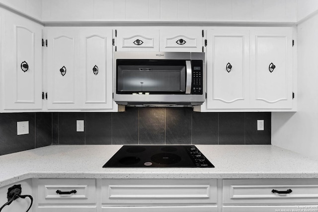 kitchen featuring decorative backsplash, light stone counters, stainless steel microwave, black electric cooktop, and white cabinetry