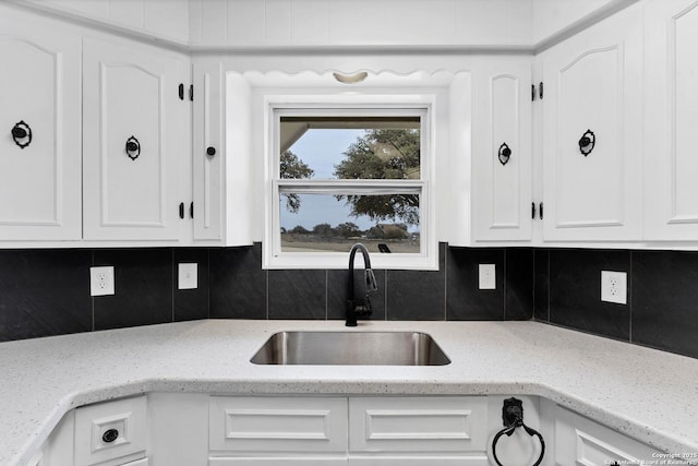 kitchen with tasteful backsplash, white cabinetry, light stone counters, and a sink