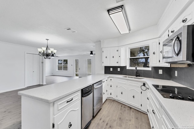 kitchen with stainless steel appliances, a peninsula, a sink, light wood-type flooring, and decorative backsplash