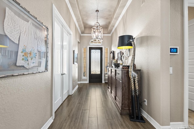 entrance foyer with baseboards, a textured wall, an inviting chandelier, wood tiled floor, and crown molding