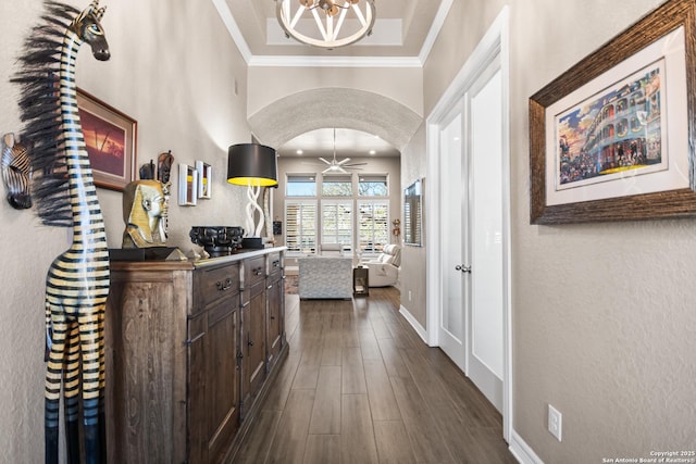 hallway with arched walkways, dark wood-style flooring, crown molding, a textured wall, and baseboards