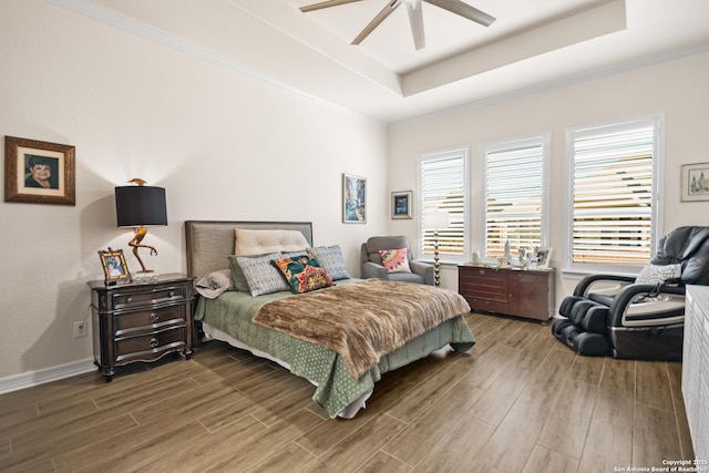 bedroom with a ceiling fan, a tray ceiling, crown molding, and wood finished floors