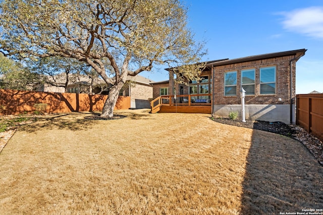 rear view of house featuring a deck, a yard, brick siding, and a fenced backyard