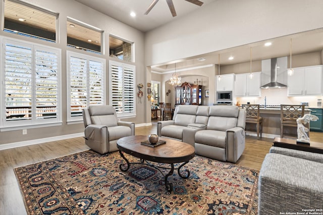 living room with a towering ceiling, light wood-style flooring, baseboards, and ceiling fan with notable chandelier