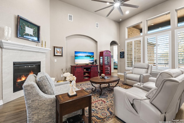 living room featuring arched walkways, a tile fireplace, wood finished floors, visible vents, and a ceiling fan