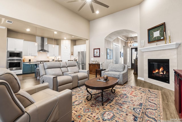 living area with arched walkways, recessed lighting, a high ceiling, wood finished floors, and a ceiling fan