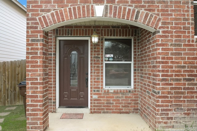 view of exterior entry featuring brick siding and fence