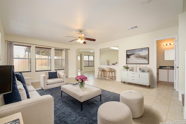 living area with light tile patterned floors, visible vents, arched walkways, baseboards, and ceiling fan