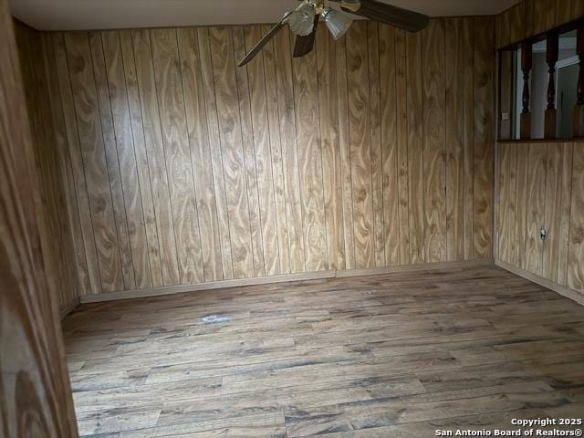 unfurnished room with ceiling fan, wood walls, and wood finished floors