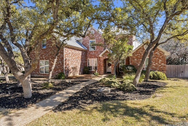 view of front facade featuring metal roof, a standing seam roof, fence, a front lawn, and brick siding