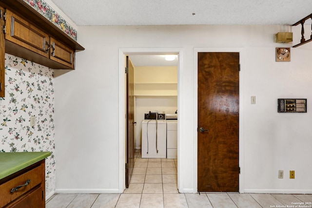 kitchen featuring baseboards, light tile patterned flooring, a textured ceiling, and washing machine and clothes dryer