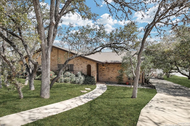 view of front of property with brick siding, roof with shingles, and a front yard