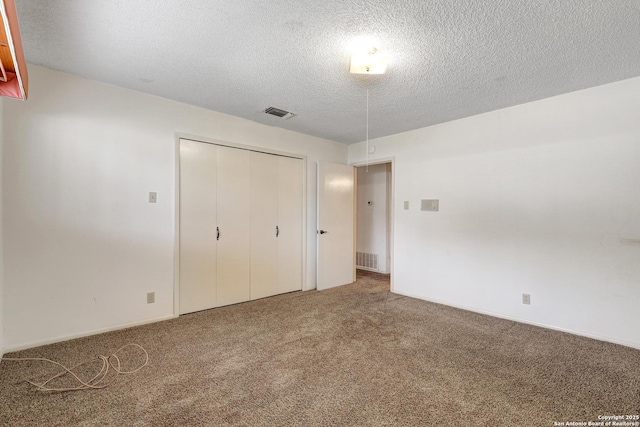 unfurnished bedroom featuring a textured ceiling, carpet floors, a closet, and visible vents