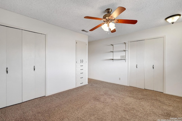 unfurnished bedroom featuring carpet, a textured ceiling, visible vents, and multiple closets