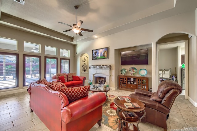 living area with baseboards, arched walkways, a ceiling fan, a raised ceiling, and a fireplace